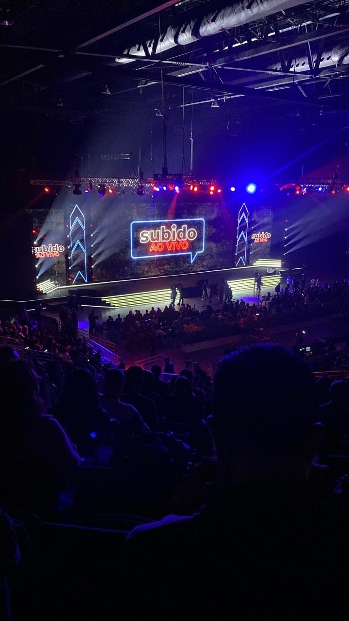 Palco do evento Subido Ao Vivo visto da plateia, com telão e luzes