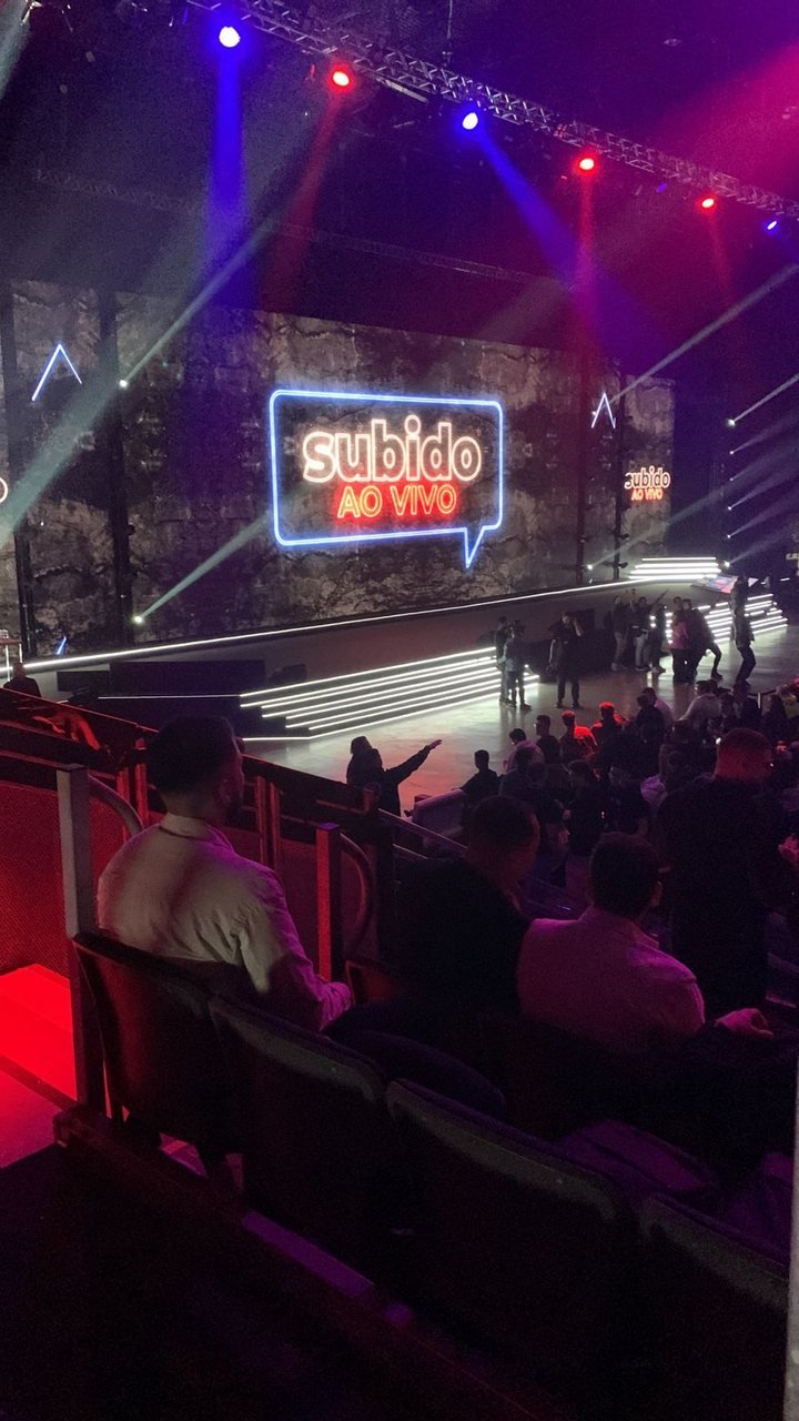 Palco e plateia do evento Subido Ao Vivo com iluminação azul e vermelha